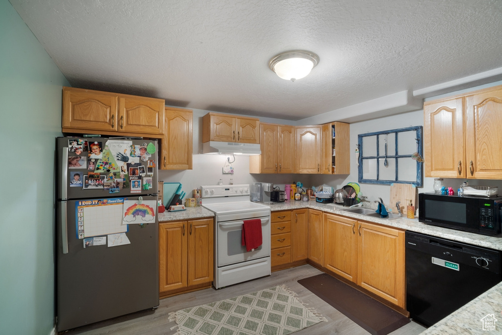 Kitchen with black appliances, under cabinet range hood, a sink, a textured ceiling, and light wood-style floors