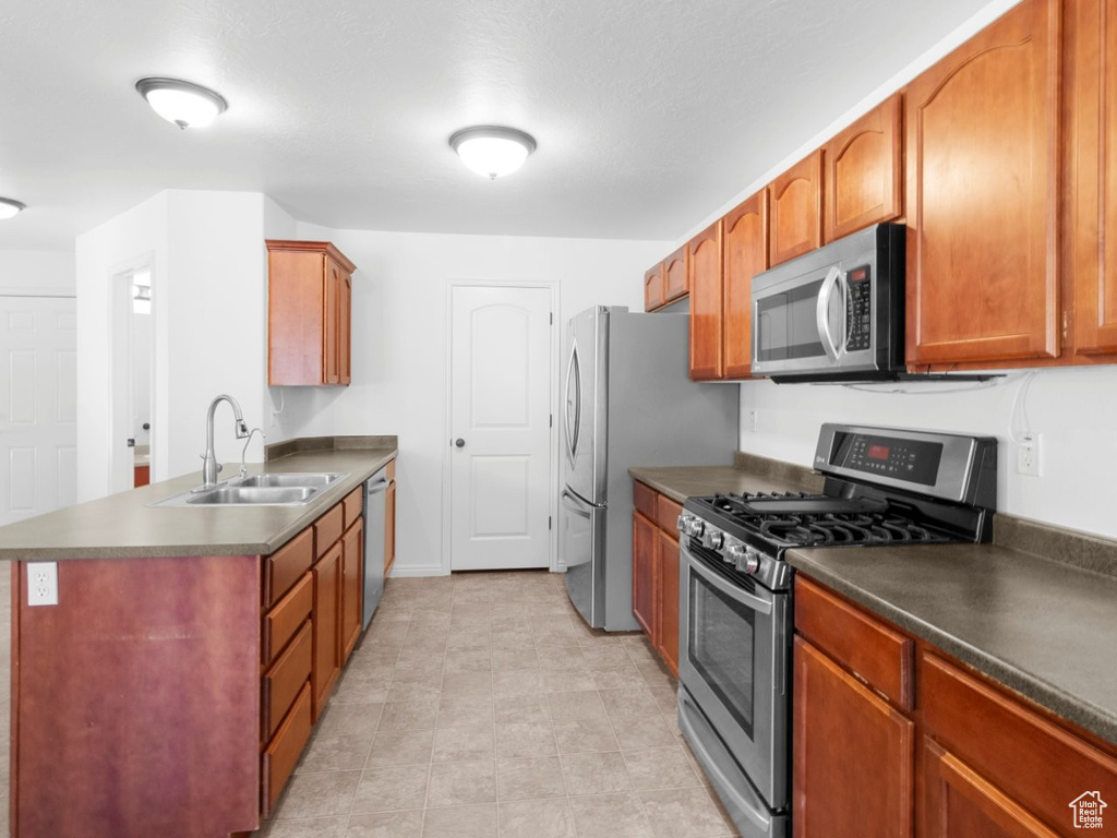 Kitchen featuring appliances with stainless steel finishes, a sink, dark countertops, and a peninsula
