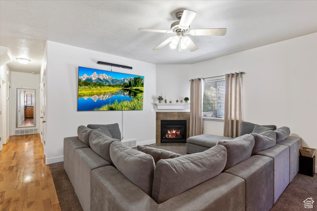 Living room featuring a textured ceiling, ceiling fan, a tiled fireplace, baseboards, and light wood finished floors