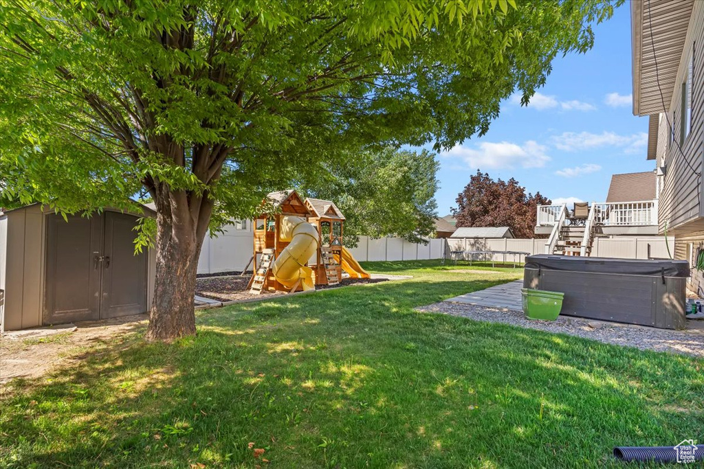 View of yard with a hot tub, a shed, a playground, and an outbuilding