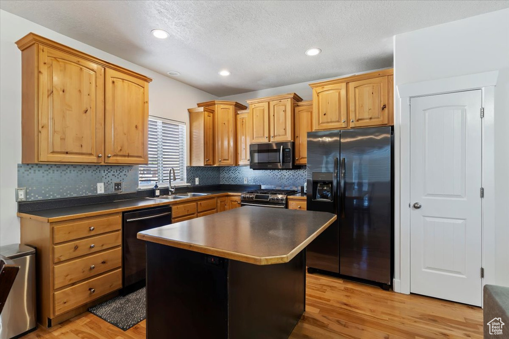 Kitchen featuring stainless steel appliances, a sink, dark countertops, decorative backsplash, and light wood finished floors