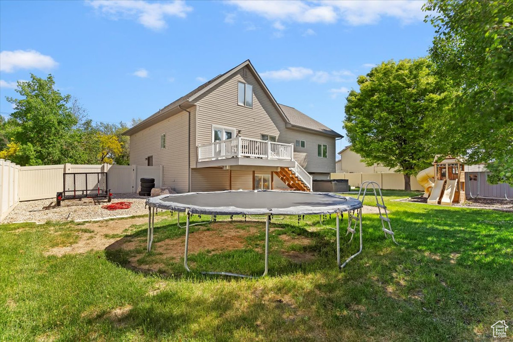 Back of property featuring a trampoline, a playground, a wooden deck, and stairs