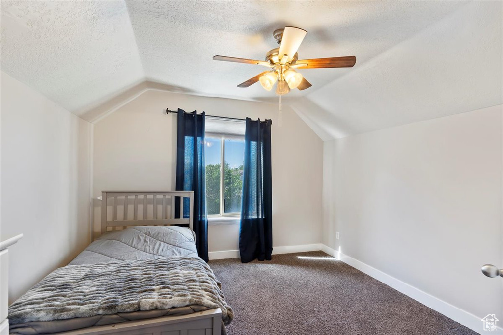 Bedroom featuring vaulted ceiling, carpet, a textured ceiling, baseboards, and a ceiling fan