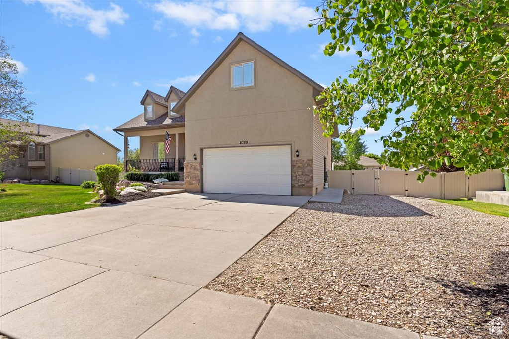 Traditional-style home with a gate, driveway, an attached garage, fence, and stone siding