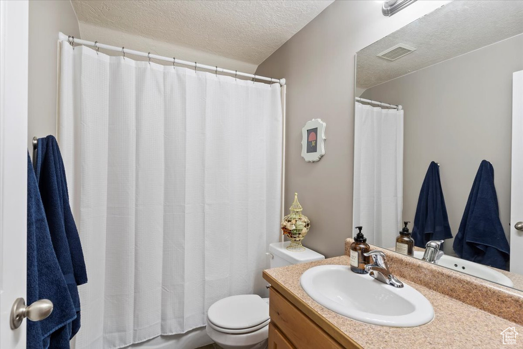 Full bathroom with a textured ceiling, toilet, vanity, and a shower with curtain
