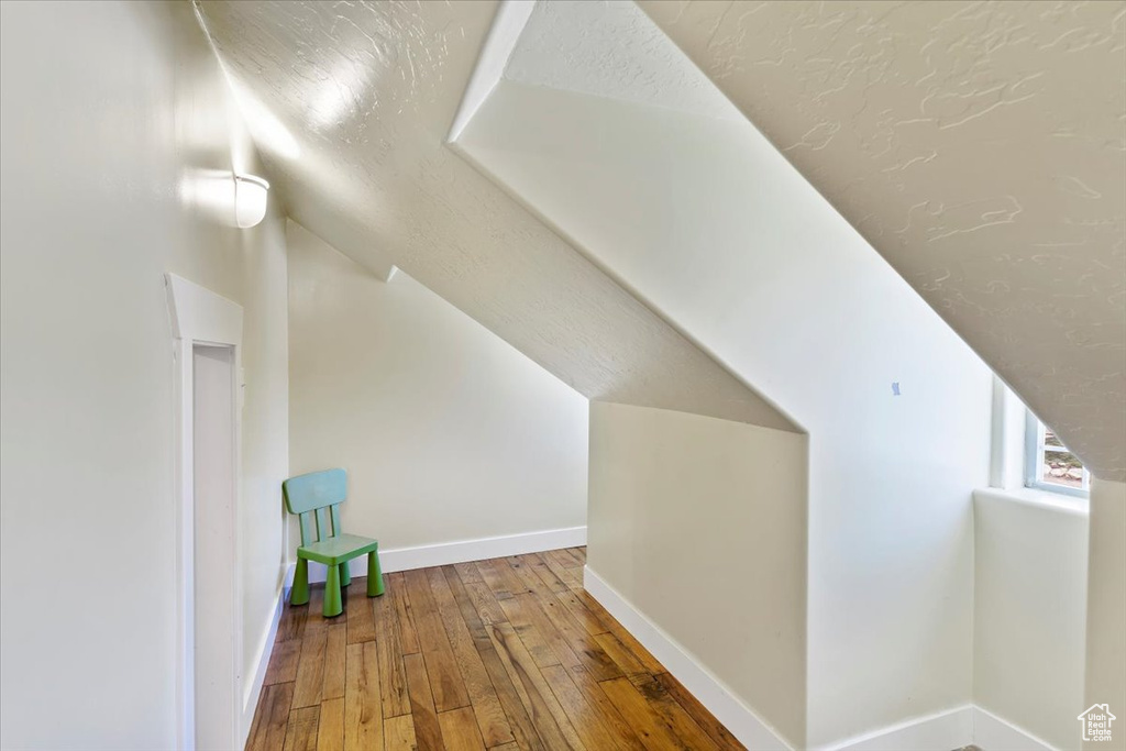 Bonus room with hardwood / wood-style flooring, vaulted ceiling, baseboards, and a textured ceiling