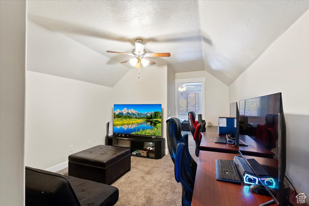 Carpeted home office with a ceiling fan, vaulted ceiling, and a textured ceiling