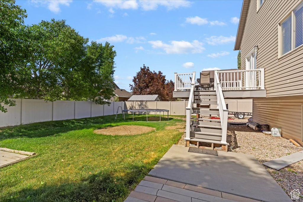 View of yard featuring a trampoline, stairs, a wooden deck, and a patio