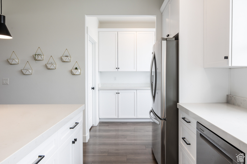Kitchen featuring appliances with stainless steel finishes, light countertops, white cabinetry, wood finished floors, and hanging light fixtures