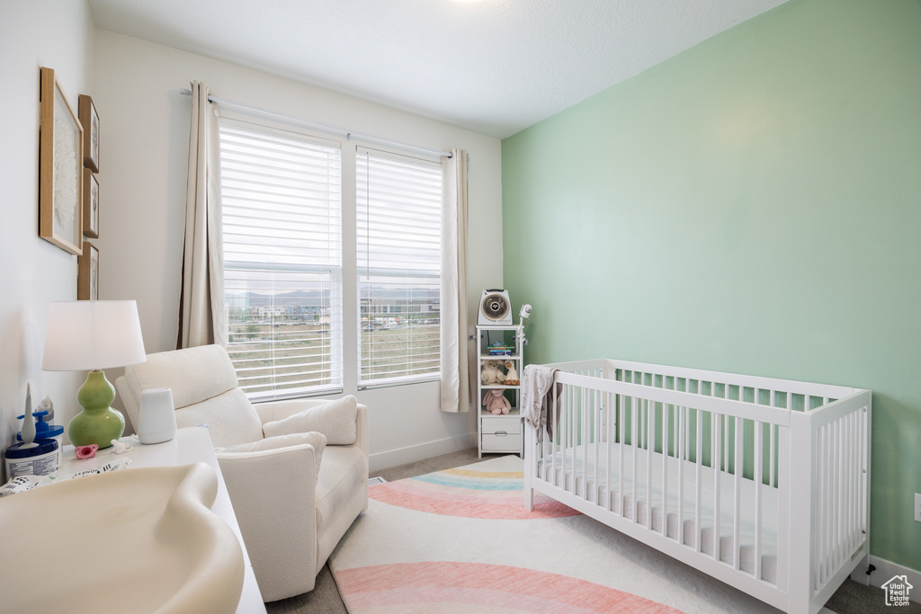 Carpeted bedroom featuring multiple windows, a nursery area, and baseboards