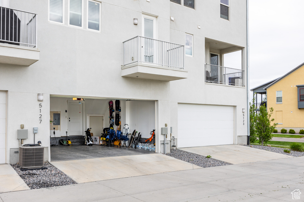 View of front facade featuring a balcony, stucco siding, a garage, driveway, and central AC
