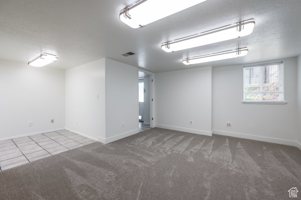 Carpeted empty room with baseboards, a textured ceiling, and tile patterned flooring