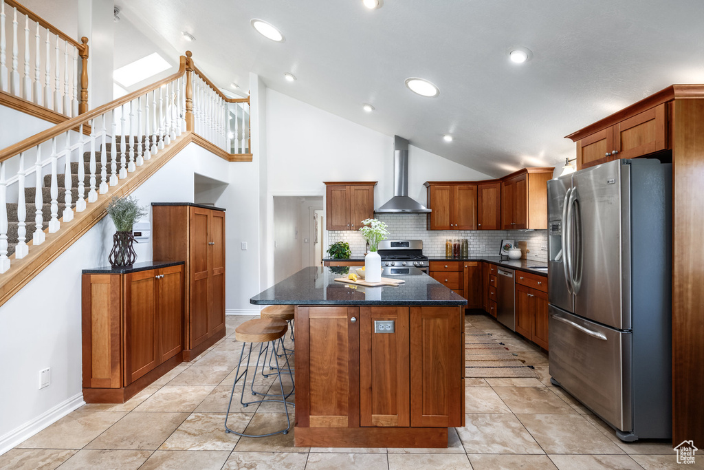 Kitchen with stainless steel appliances, wall chimney exhaust hood, a center island, high vaulted ceiling, and brown cabinetry