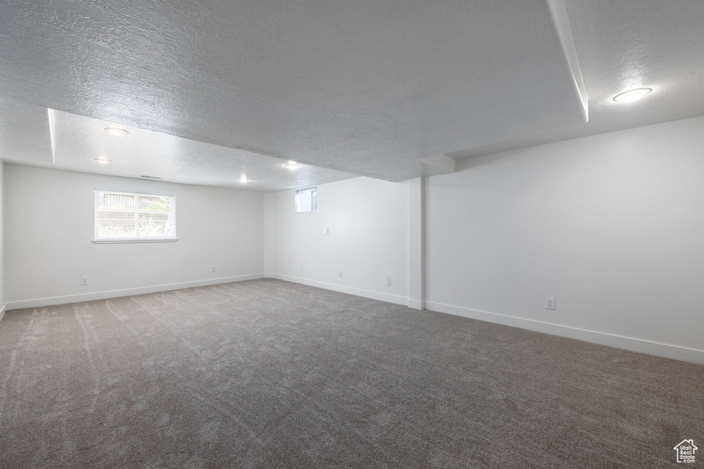 Basement featuring a textured ceiling, carpet flooring, and baseboards