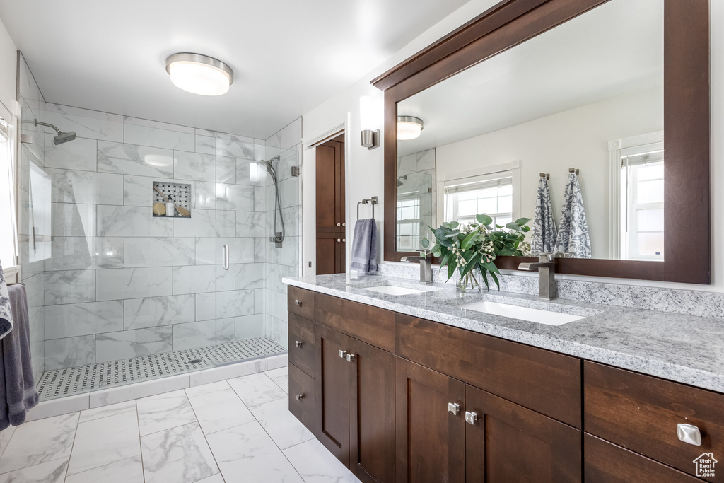 Full bath featuring marble finish flooring, a shower stall, and double vanity