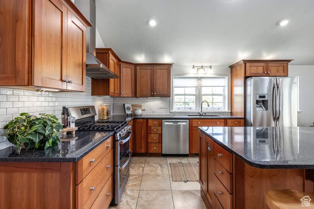 Kitchen featuring appliances with stainless steel finishes, a sink, brown cabinetry, backsplash, and dark stone countertops