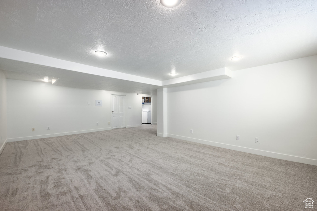Finished below grade area with baseboards, a textured ceiling, and light colored carpet