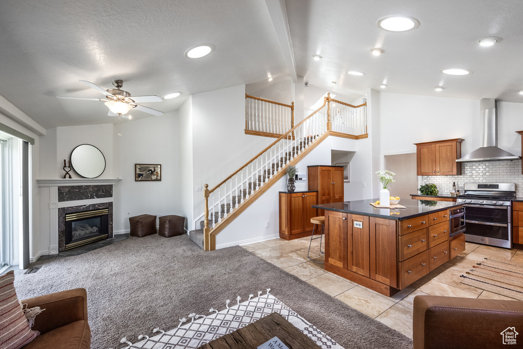 Kitchen with wall chimney exhaust hood, double oven range, open floor plan, brown cabinetry, and dark countertops