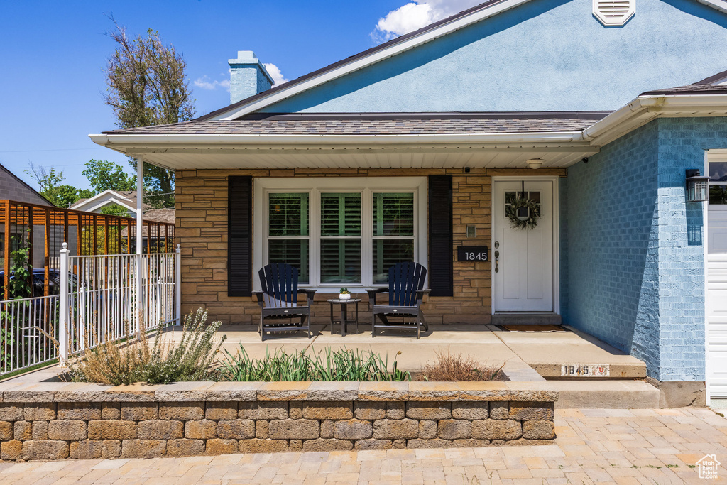 Entrance to property with covered porch, fence, a chimney, roof with shingles, and stone siding