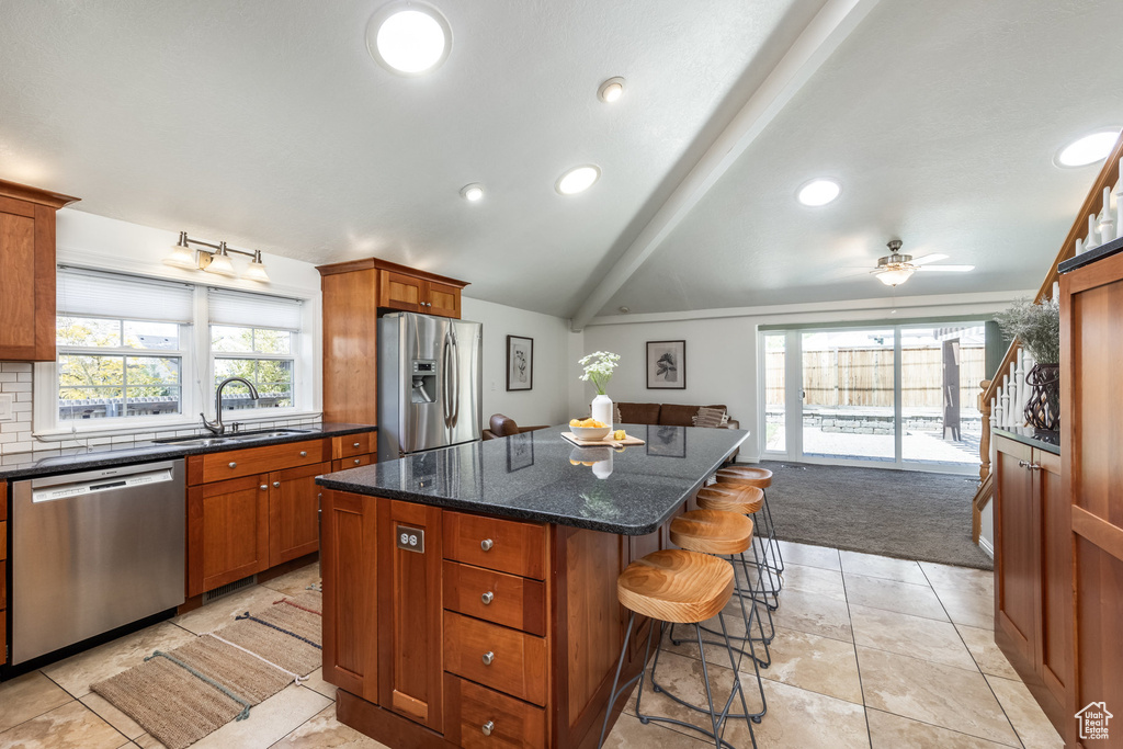 Kitchen with appliances with stainless steel finishes, a sink, a center island, brown cabinets, and a breakfast bar area