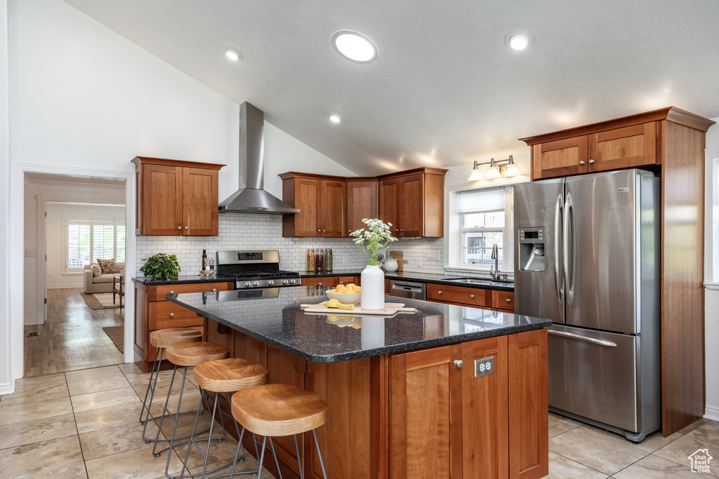 Kitchen featuring stainless steel appliances, wall chimney range hood, a sink, lofted ceiling, and decorative backsplash
