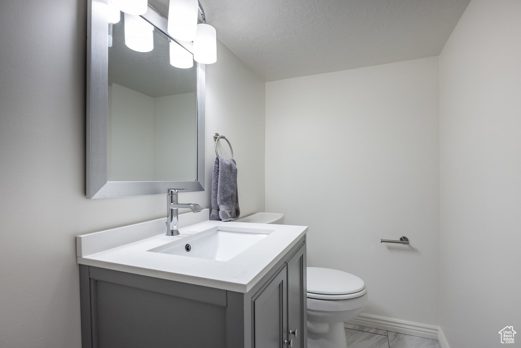 Bathroom featuring vanity, toilet, marble look tiles, and baseboards