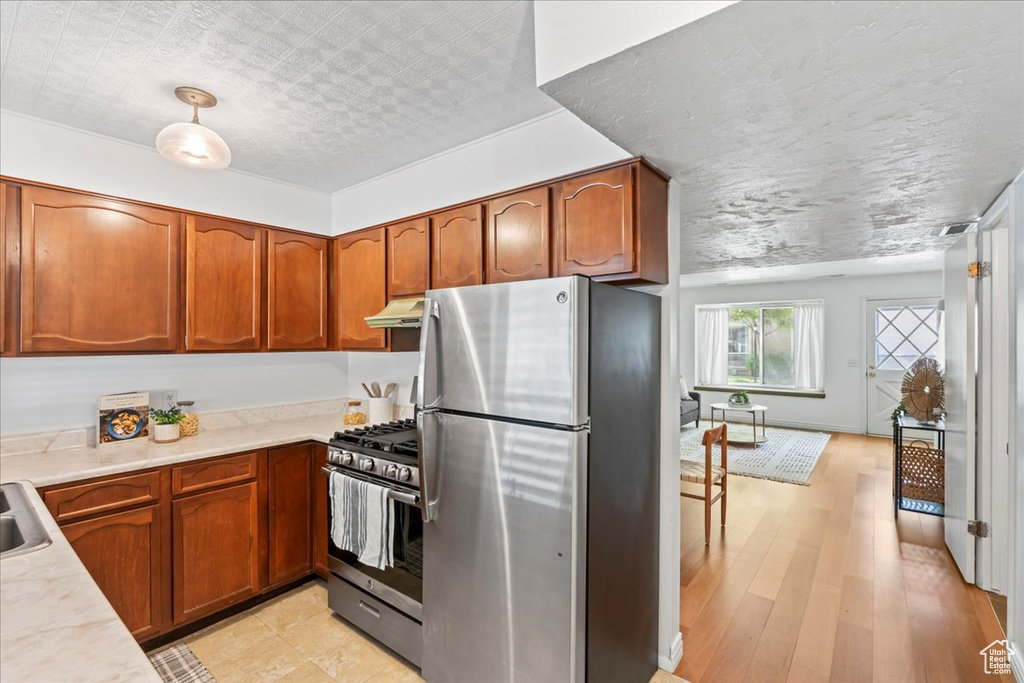 Kitchen featuring appliances with stainless steel finishes, under cabinet range hood, light countertops, and brown cabinetry