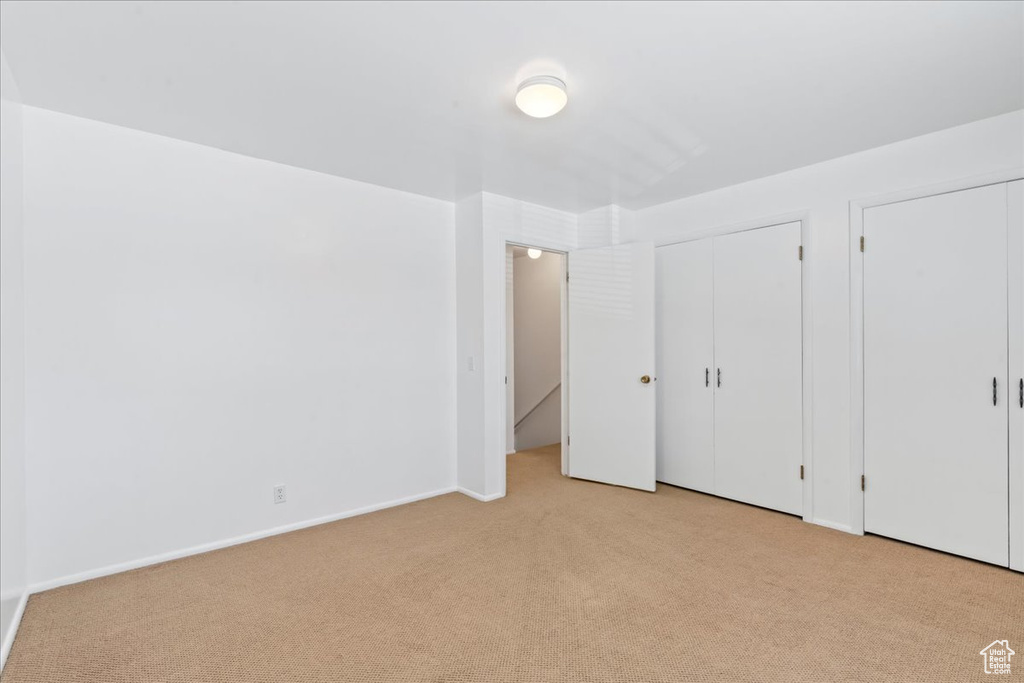 Unfurnished bedroom with light carpet, multiple closets, and baseboards
