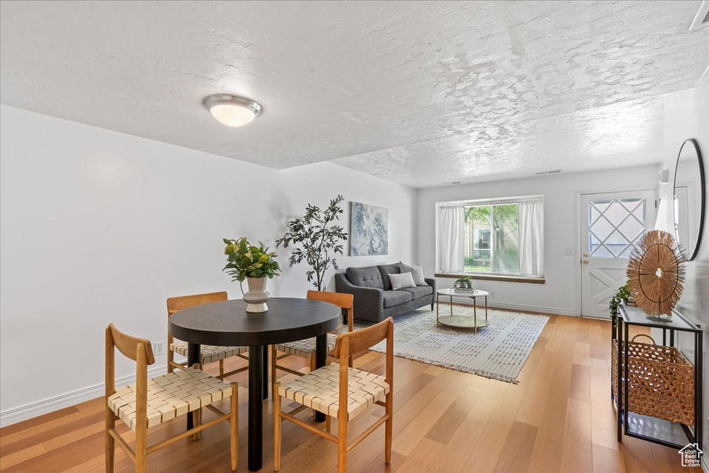 Dining area with a textured ceiling, light wood-type flooring, and baseboards