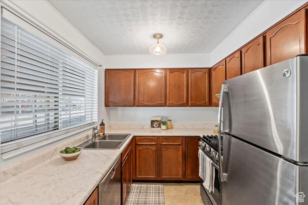 Kitchen with appliances with stainless steel finishes, a sink, light countertops, and brown cabinetry