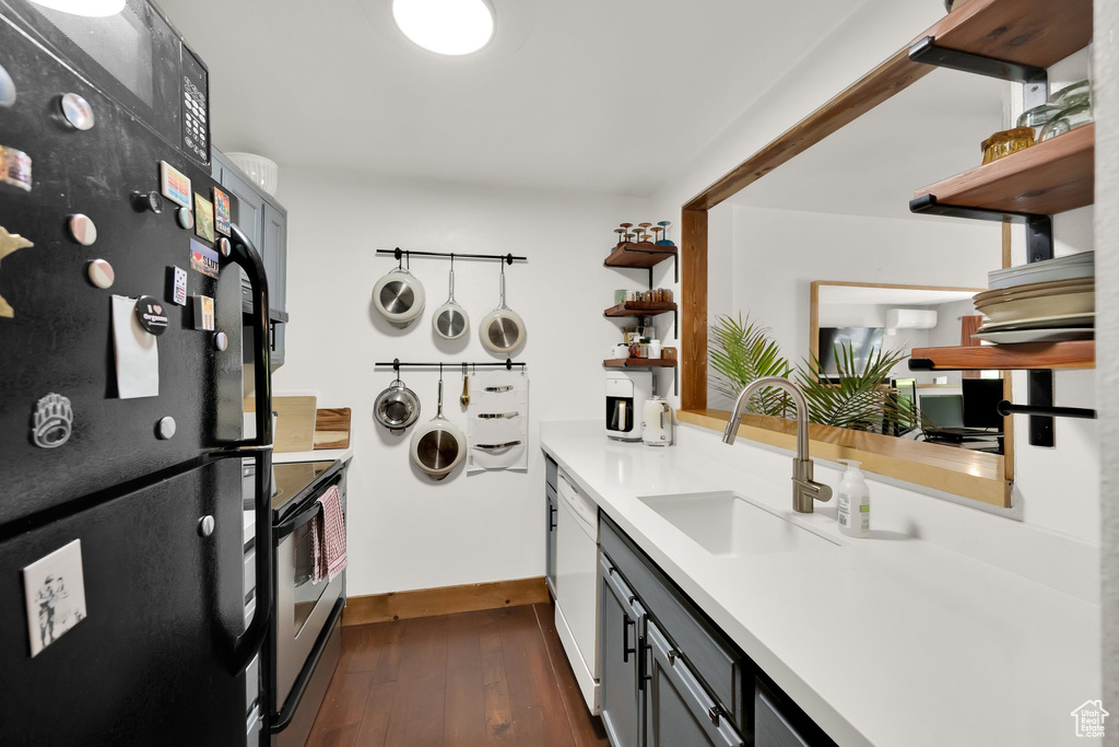 Kitchen featuring open shelves, freestanding refrigerator, a sink, light countertops, and dark wood-type flooring