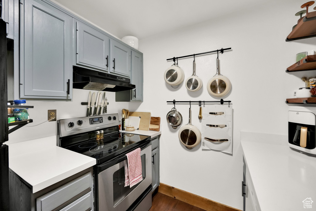 Kitchen with stainless steel range with electric cooktop, under cabinet range hood, open shelves, light countertops, and dark wood-type flooring
