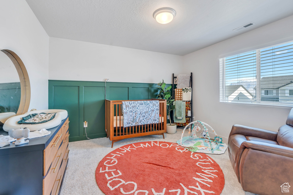 Bedroom with a decorative wall, light carpet, a crib, and wainscoting