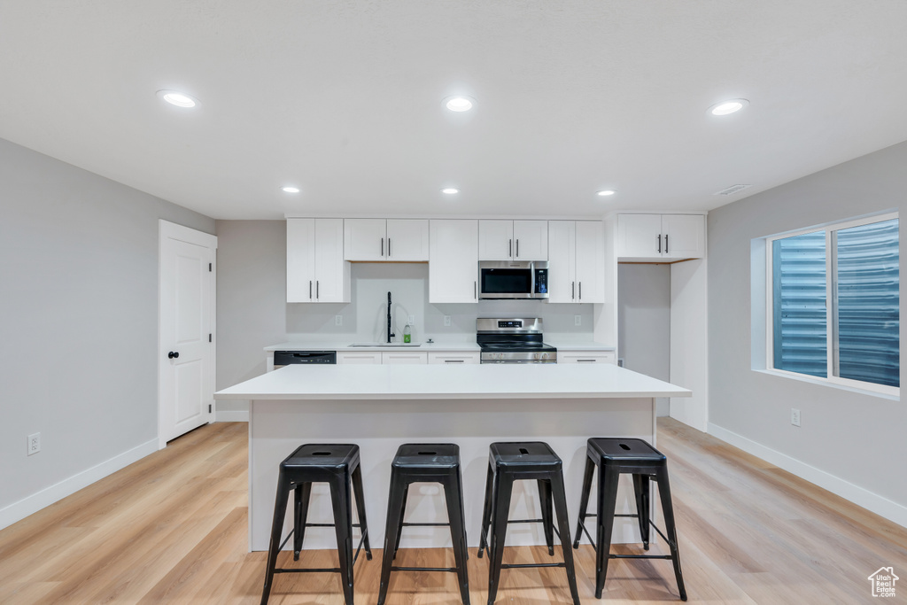 Kitchen featuring appliances with stainless steel finishes, a sink, a breakfast bar area, white cabinetry, and recessed lighting