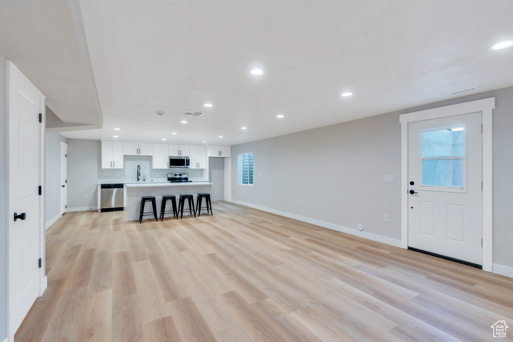 Unfurnished living room with a sink, baseboards, recessed lighting, light wood-style floors, and healthy amount of natural light