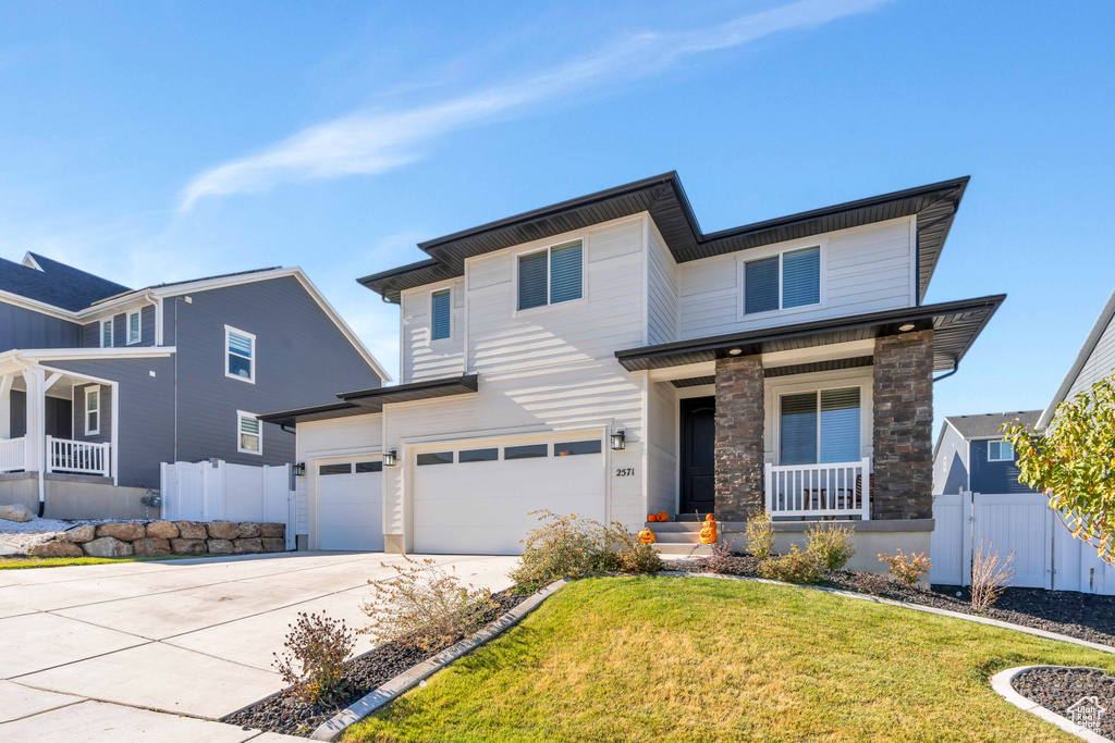 View of front of property featuring a porch, a garage, driveway, and stone siding