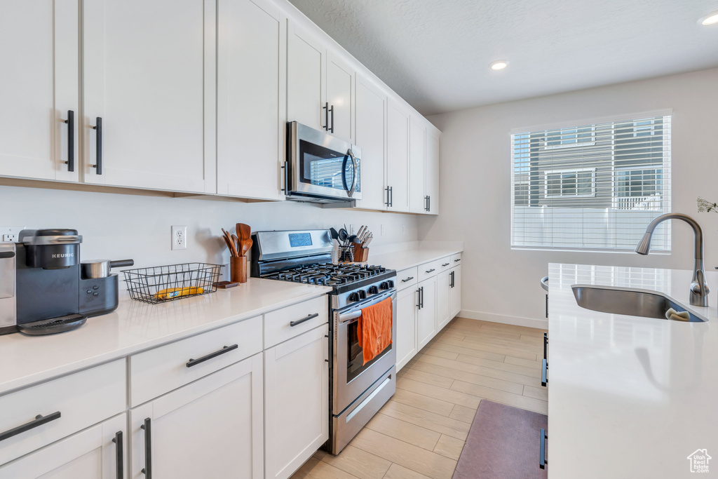 Kitchen with appliances with stainless steel finishes, a sink, white cabinets, baseboards, and light countertops