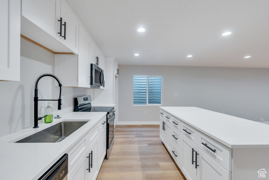 Kitchen with appliances with stainless steel finishes, a sink, light wood-style flooring, recessed lighting, and white cabinets
