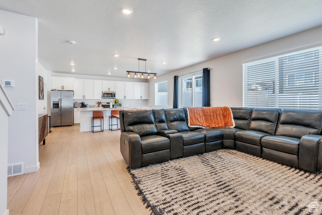 Living room with light wood-style flooring, recessed lighting, a textured ceiling, and baseboards