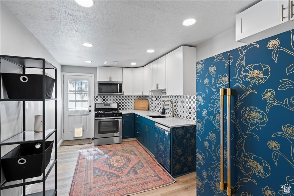 Kitchen featuring appliances with stainless steel finishes, a sink, a textured ceiling, light wood-style flooring, and light countertops