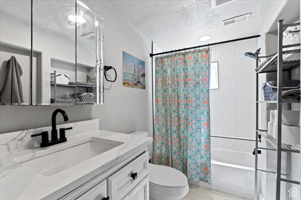 Bathroom with toilet, marble finish flooring, shower / bath combo with shower curtain, a textured ceiling, and vanity