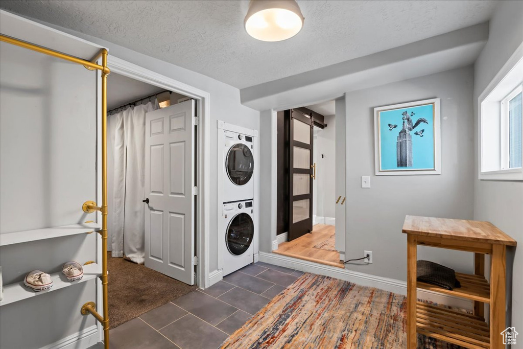 Washroom featuring stacked washer and clothes dryer, a textured ceiling, dark tile patterned flooring, and baseboards