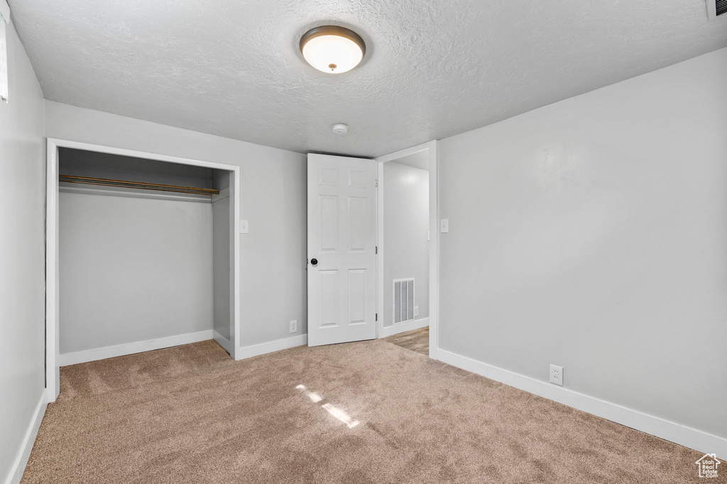 Unfurnished bedroom featuring a textured ceiling, carpet flooring, baseboards, and a closet