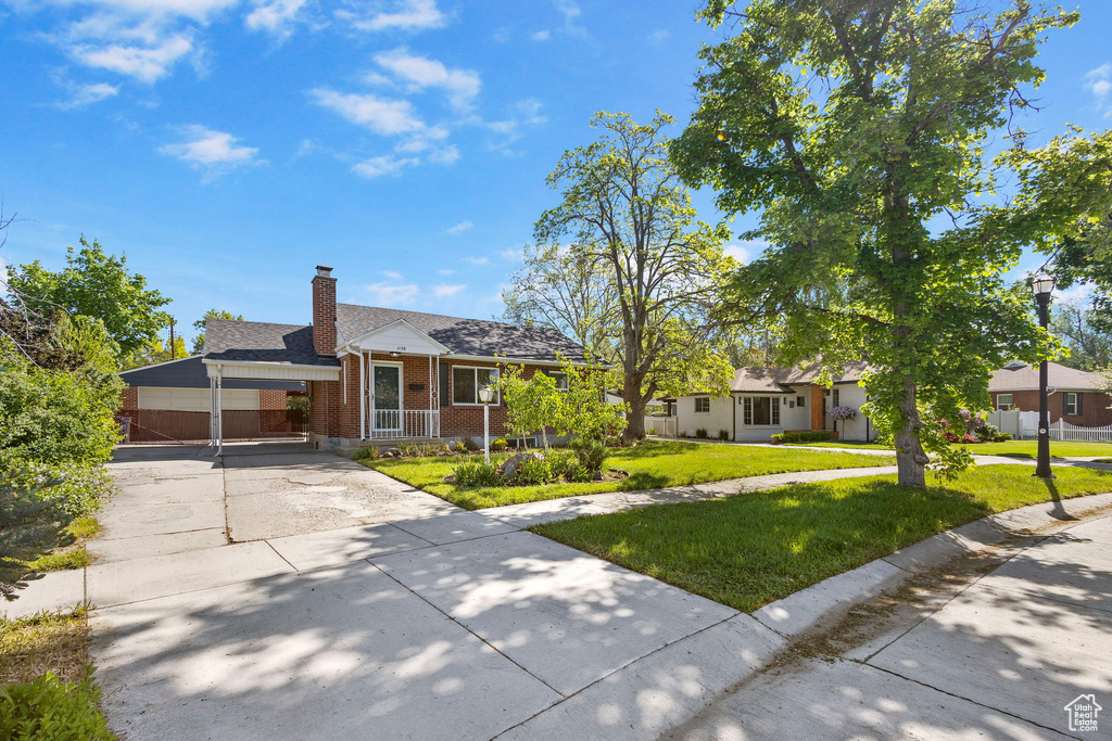 View of front of home with driveway, brick siding, a front yard, a chimney, and an attached carport