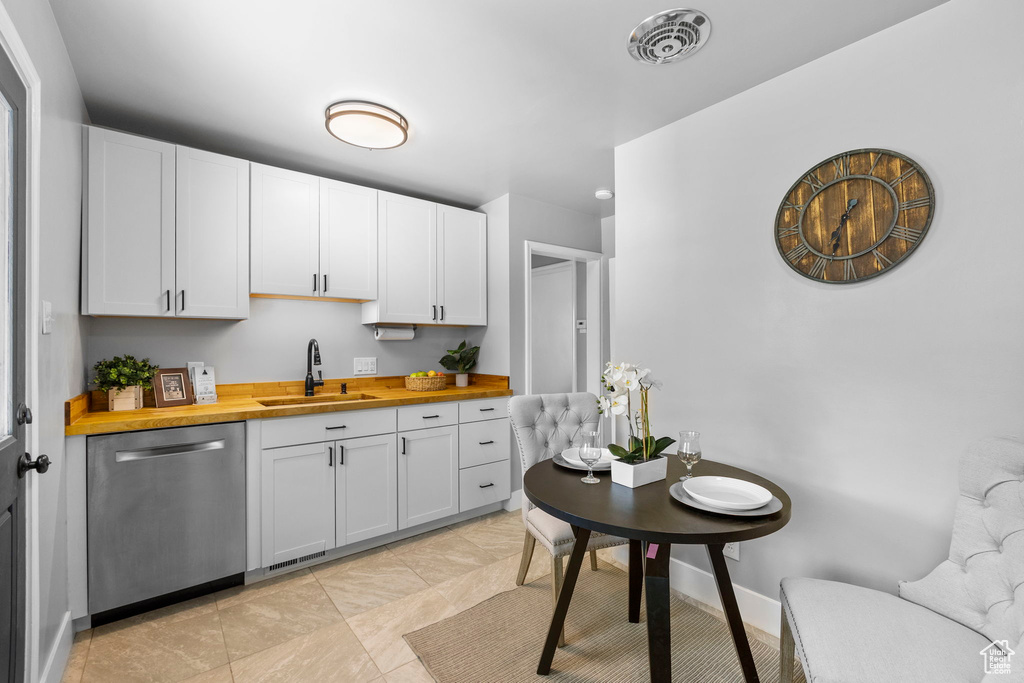 Kitchen featuring stainless steel dishwasher, wood counters, a sink, white cabinetry, and light tile patterned flooring