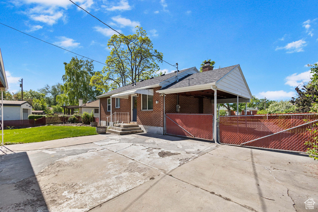 View of side of property featuring brick siding, a gate, roof with shingles, and a chimney