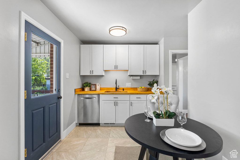 Kitchen with a sink, butcher block counters, dishwasher, white cabinets, and baseboards
