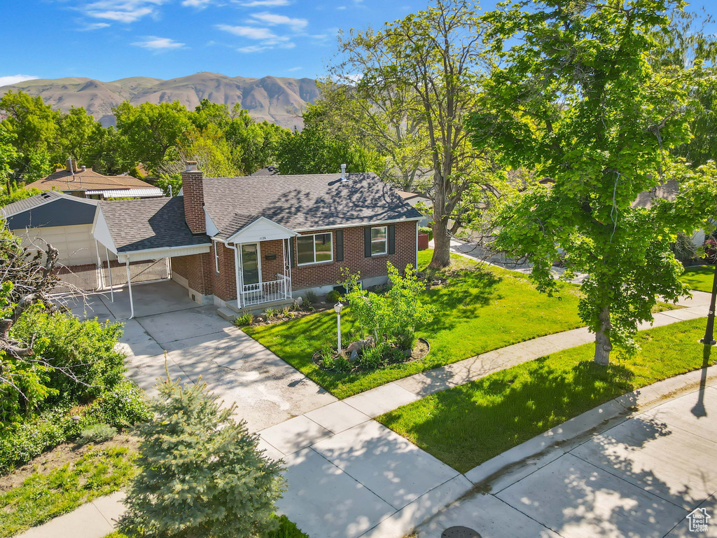 View of front of property with brick siding, concrete driveway, a chimney, a front lawn, and roof with shingles