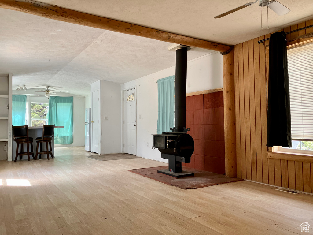 Unfurnished living room featuring ceiling fan, a wood stove, wood finished floors, healthy amount of natural light, and lofted ceiling
