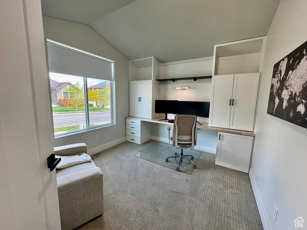 Home office featuring light carpet, built in desk, baseboards, and lofted ceiling